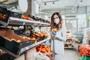 Young pretty woman choosing fruits in the grocery store, wearing mask and medical gloves for protection during virus epidemic. Health, safety and pandemic concept 
