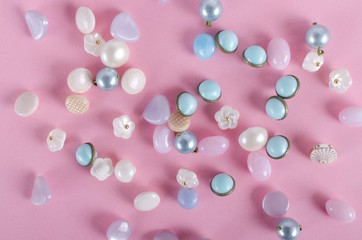 Top view of pastel colored buttons on the pink surface. Different shapes of buttons as a background