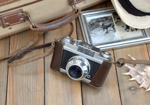 retro camera with picture frame, hat suitcase and seashell on wooden table