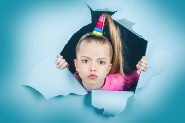 Child girl looking out of a paper hole. Banner. Happy girl. View of girl face through hole in blue...