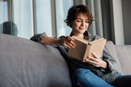 Image of brunette cute focused woman reading book and smiling