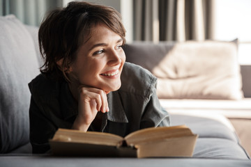 Image of caucasian cute pleased woman reading book and smiling