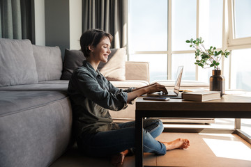 Image of nice young cheerful woman using laptop and smiling