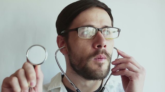 Young beautiful doctor checks the serviceability of the stethoscope, while preparing for the examination of patients. A young doctor blows on a stethoscope checking his condition.