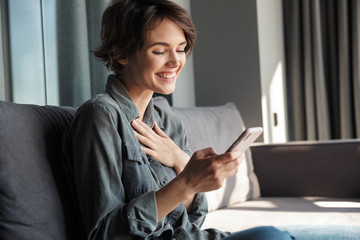 Image of beautiful young joyful woman using mobile phone and laughing