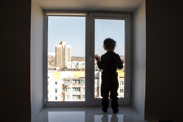 Fototapeta premium stay at home. A child stands on a windowsill and looks at an empty deserted street during the worldwide quarantine of the coronavirus pandemic.