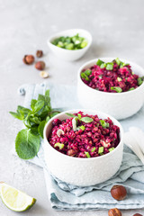 White ceramic bowls with buckwheat, beetroot, nuts and herbs warm salad, light grey concrete background. Dietary balanced food concept. Vegetarian and vegan meal. 