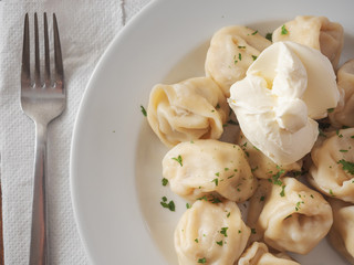 Traditional russian large dumplings with sour cream on a white plate and wooden table, and a metal fork.