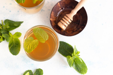 Fresh hot peppermint herbal tea in glasses with fresh mint leaves and honey on light blue stone...