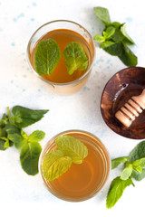 Fresh hot peppermint herbal tea in glasses with fresh mint leaves and honey on light blue stone background. Moroccan tea with mint. Top view.