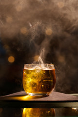 A glass of smoked whiskey on a table with cubes of ice side view