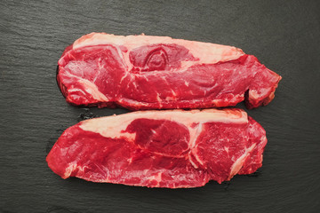 Two fresh striploin steaks on a black slate plate. Raw meat product.