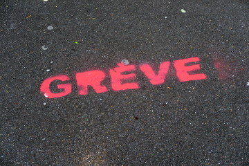 Inscription GREVE peinte à la peinture rose sur le sol de goudron noir dans la rue.