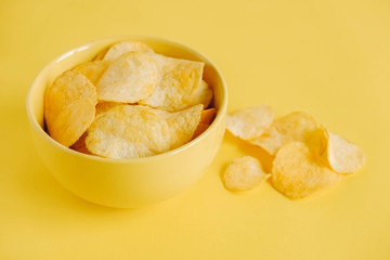 Potato chips in a yellow bowl on a yellow background. Copy, empty space for text