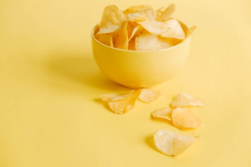 Potato chips in a yellow bowl on a yellow background. Copy, empty space for text