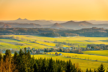 Hilly landscape illuminated by evening sunset. Green grass fields and hills on the horizont. Vivid spring rural countryside, Czech Republic