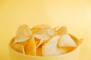 Potato chips in a yellow bowl on a yellow background. Copy, empty space for text