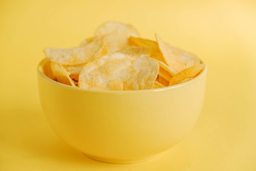 Potato chips in a yellow bowl on a yellow background. Copy, empty space for text