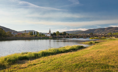 Bridge Ponte de Lima with church during afternoon on sunny day, river Lima and green grass on riverside, Portugal.