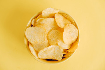 Potato chips in a yellow bowl on a yellow background. Top view. Copy, empty space for text