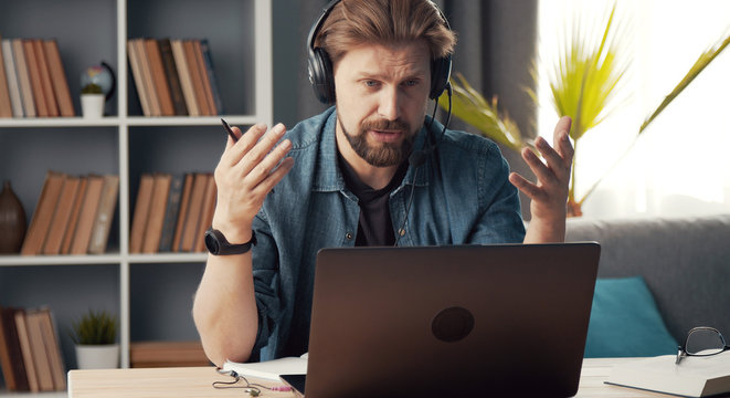 Adult man working remotely sitting at laptop with headset on staying in flat during quarantine
