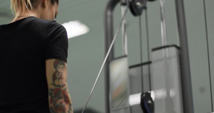 woman exercising with Cable triceps bar at gym.Rear view, slow motion. Woman training at triceps pushdown machine