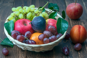 red grape berries and fresh fruits in a straw basket on a dark wooden background.