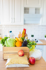 A wooden box of different food, fruit, vegetables, oil, water, sugar on the kitchen. Safe home delivery.