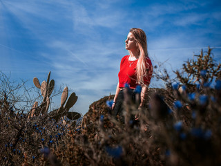 full length portrait of a pensive young woman with red shirt and blond hair in the forest surrounded by nature