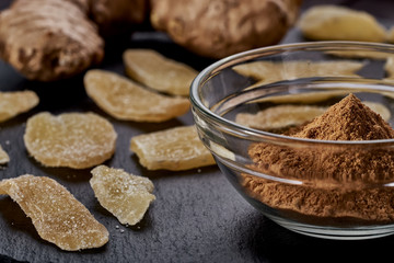 A clear plate with ground ginger, the side lies ginger slices dried fruit and a whole ripe ginger on a stone black plate. Against viruses and diseases. immune product