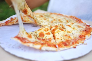 In selective fous pan of pizza with  cheese stretches between pizza and a piece,blurred a female hand 