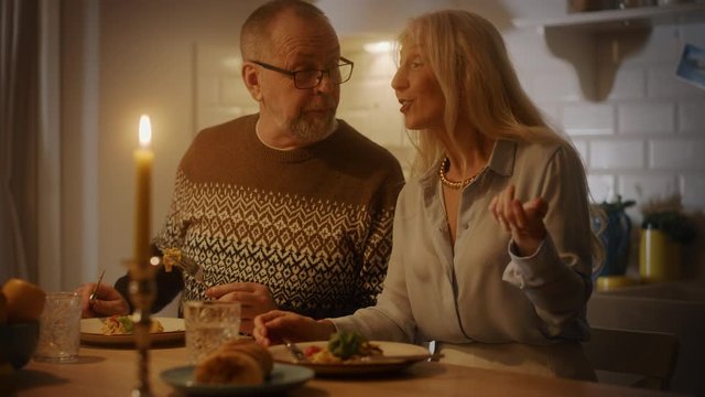 Happy Senior Couple in Love Have Romantic Evening, Eating Delicious Dinner Meal in the Kitchen, Celebrating Anniversary. Elderly Have Romantic Evening with Wine, Festive Table in Cozy Kitchen Interior