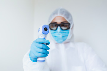 Naklejka premium Doctor holding infrared thermometer. Portrait of medical professional in protective clothing measuring contactless fever at Covid-19 test center during coronavirus epidemic.