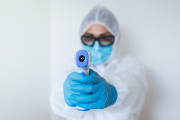 Doctor holding infrared thermometer. Portrait of medical professional in protective clothing...