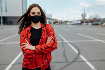 Girl in a medical mask sits on a bench on the street. Portrait of a girl in a mask on the street. Coronavirus pandemic concept. Mask in the street.