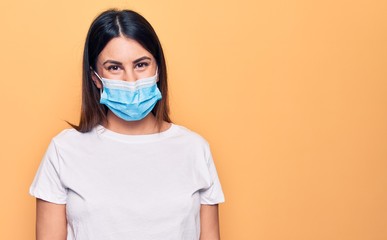 Young woman wearing protection mask for coronavirus disease over yellow background with a happy and cool smile on face. Lucky person.