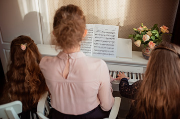 Home piano lesson. A woman and two girls practice sheet music on one musical instrument. Family concept. The idea of activities for children during quarantine.