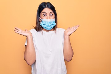 Young woman wearing protection mask for coronavirus disease over yellow background clueless and confused with open arms, no idea and doubtful face.