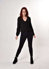Portrait of a pretty girl with red hair wearing black jeans, boots and a blouse.  full length...