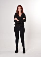 Portrait of a pretty girl with red hair wearing black jeans, boots and a blouse.  full length standing pose, facing the camera, on a studio background.