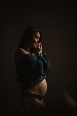 Young beautiful pregnant woman standing near window at home, dark style 