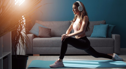 Fitness girl in athletic clothes and headphones doing forward lunge training leg muscles in flat