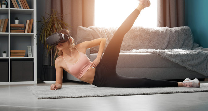 Slim girl in VR and activewear side-lying on floor raising one leg up doing fitness exercises in apt
