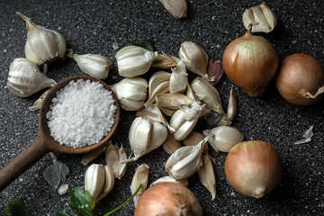 Large salt in a wooden spoon, onion, garlic are on the table.