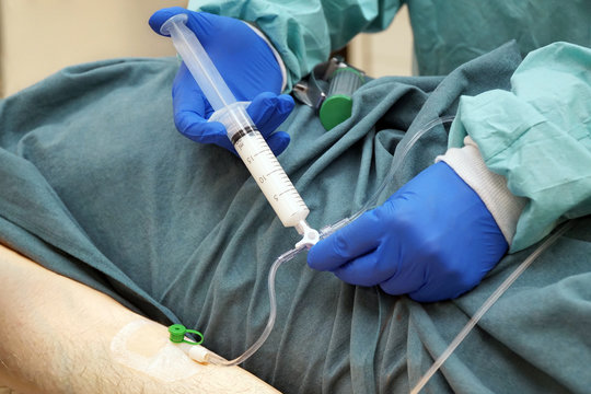 Arzt in OP h&auml;lt spritzt einem Patienten Narkosemittel oder Sedativum