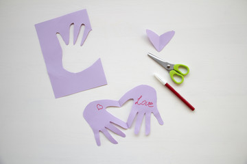 Child made a greeting card. Step 7. Child holds a card in his hands. Tools and materials for children's art creativity on table. Mother's day or March 8 greeting card DIY idea. 