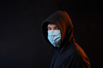 portrait young guy in black hoodie on medicine mask on black background