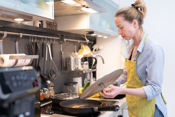 Stay at home housewife woman cooking in kitchen, stir frying dish in a saucepan, preparing food for...
