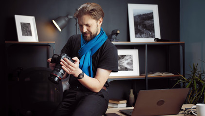 Half-length shot of photographer reviewing taken pics in DSLR camera sitting on table in studio