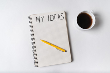 Notepad with words MY IDEAS. Pen and cup of coffee. Top view. White background